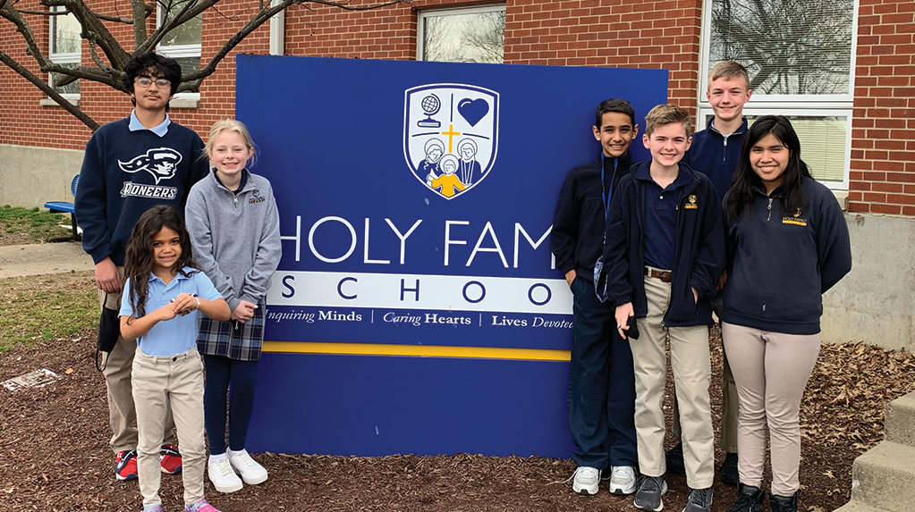 students standing together in front of holy family school sign